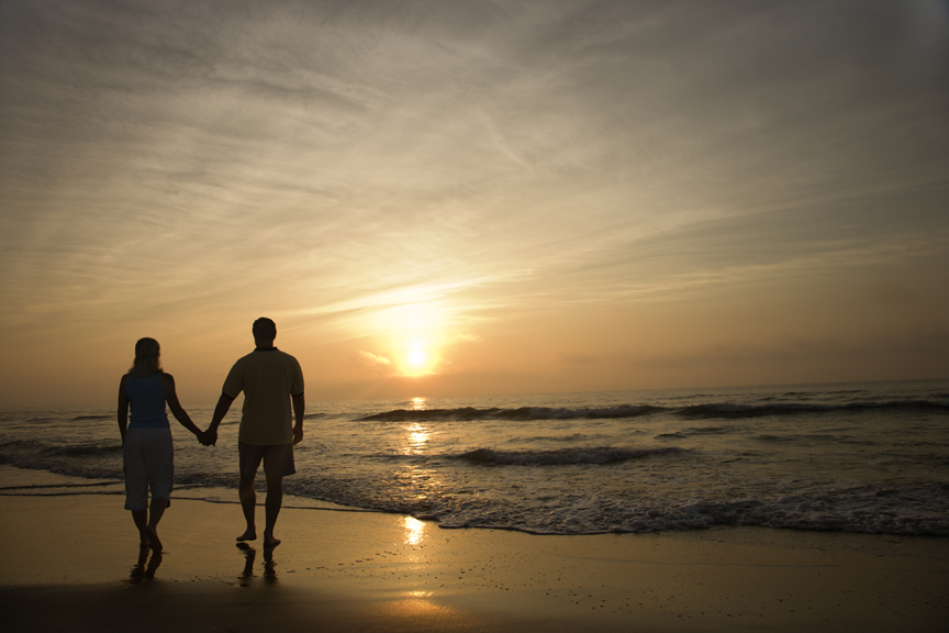 Couple holding hands on beach at sunset