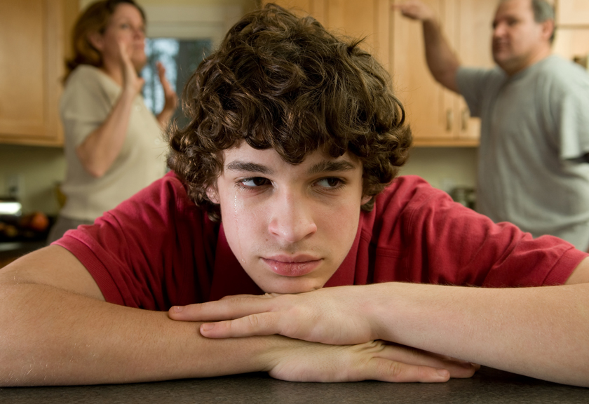 Teenager appearing sad while adults fight in the background