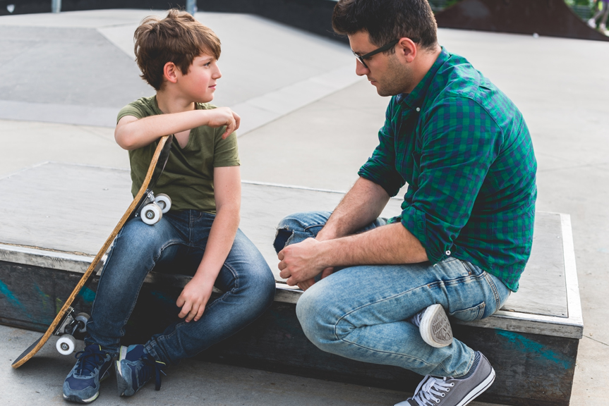 Father speaking with son at skateboard park