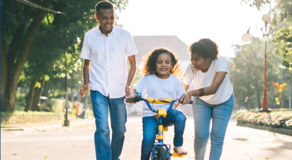 Girl on bike with parents helping.